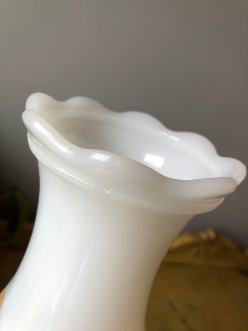 May include: White milk glass vase with a scalloped rim. The vase has a flared opening and a narrow base.