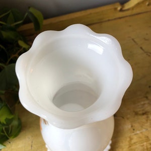 May include: White milk glass vase with a scalloped rim and a beaded base. The vase has a simple, elegant design.