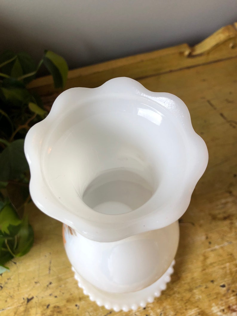 May include: White milk glass vase with a scalloped rim and a beaded base. The vase has a simple, elegant design.