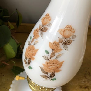 May include: White milk glass lamp with a gold base and a floral design featuring brown and orange roses.