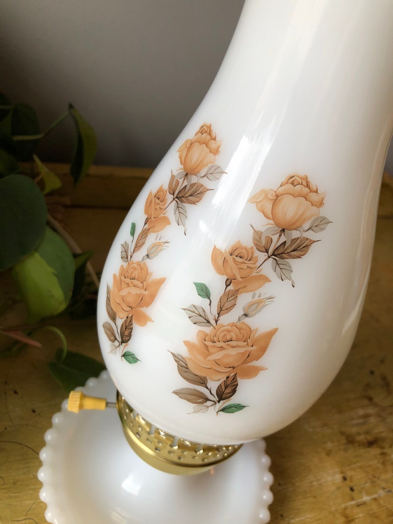 May include: White milk glass lamp with a gold base and a floral design featuring brown and orange roses.