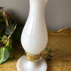 May include: White milk glass lamp with a gold metal base and a scalloped top. The lamp has a beaded base.