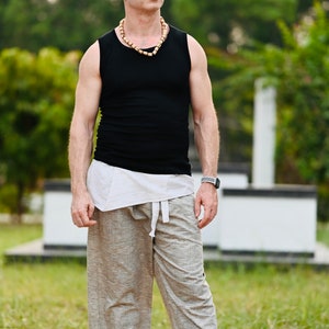 May include: A person wearing a black tank top, light-colored pants, and a wooden bead necklace. The pants are a light gray color. The person is also wearing a watch and sandals.