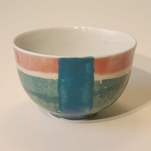 Pode incluir: Uma pequena tigela de cerâmica branca com um design geométrico verde, azul e rosa.