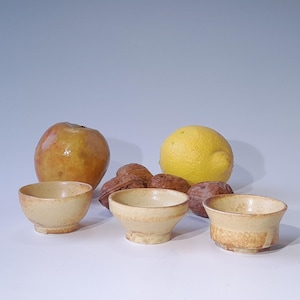 May include: Four small, yellow ceramic bowls with a brown glaze. The bowls are arranged in a row on a white surface. There are walnuts and a lemon in the background.
