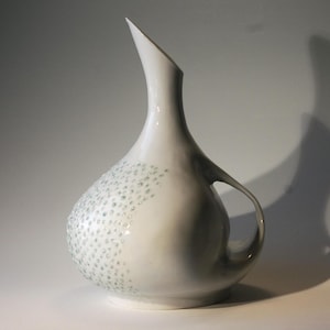 May include: A white ceramic jug with a long, curved spout and a handle. The jug has a speckled design in shades of blue and white.
