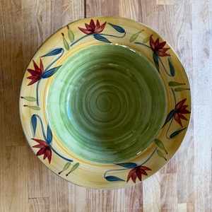 May include: A decorative ceramic bowl with a floral design. The bowl features a green interior, a yellow rim, and is adorned with red flowers and blue leaves. The bowl is approximately 12 inches in diameter.