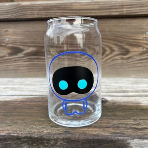 May include: A clear glass can with a blue and black cartoon robot design. The robot has a round head with two large blue eyes and a small mouth.