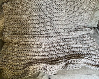 May include: A large, beige crocheted throw blanket with a textured, chunky knit pattern. The blanket is draped over a sofa.