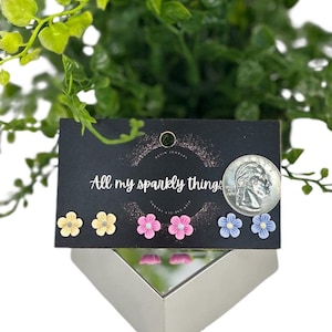 May include: A set of six flower stud earrings on a black card with the text "All my sparkly things". The earrings are in three colors: yellow, pink, and blue.