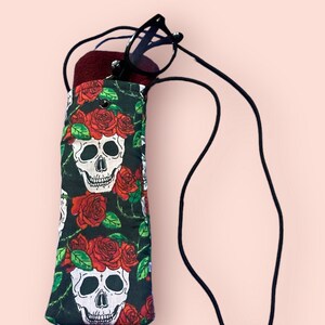 May include: A black eyeglass case with a skull and red roses print. The case has a black drawstring closure and a black cord for carrying.
