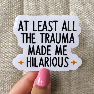 May include: White sticker with black text that reads "At least all the trauma made me hilarious" with two orange star accents.