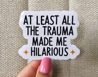 May include: White sticker with black text that reads "At least all the trauma made me hilarious" with two orange star accents.