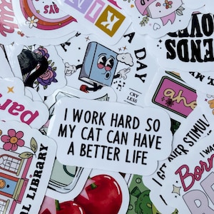 May include: A collection of colorful stickers with various designs and text. Some stickers feature phrases like "I work hard so my cat can have a better life" and "Friends Love". Other stickers have illustrations of books, flowers, and rainbows.