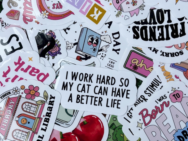 May include: A collection of colorful stickers with various designs and text. Some stickers feature phrases like "I work hard so my cat can have a better life" and "Friends Love". Other stickers have illustrations of books, flowers, and rainbows.