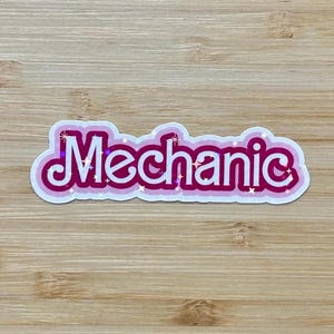 May include: A sticker with the word "Mechanic" in a bubble letter style. The word is in white with a pink outline and a light pink shadow. The sticker has a glittery effect.