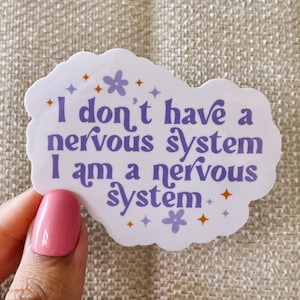 Może przedstawiać: Biała naklejka w kształcie fioletowej chmury z tekstem "I don't have a nervous system I am a nervous system" w fioletowym kolorze. Naklejka ma małe pomarańczowe i fioletowe gwiazdki i kwiaty wokół tekstu.
