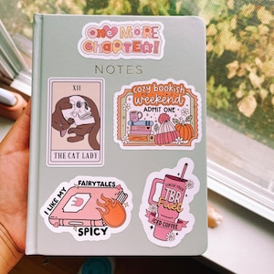 Może przedstawiać: Zbi&oacute;r kolorowych naklejek z ilustracjami książek, kawy i kota trzymającego czaszkę. Naklejki mają tekst: "One More Chapter!" "Notes" "Cozy Bookish Weekend" "Admit One" "The Cat Lady" "Fairytales" "I Like My Spicy" "Finish Your TBR Fuel" "Iced Coffee"