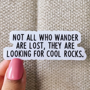May include: White sticker with black text that reads "Not all who wander are lost, they are looking for cool rocks."