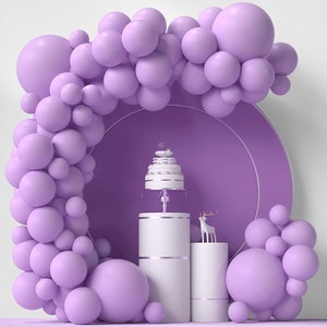 May include: A purple balloon arch with a white cake on a stand and two white pedestals. A small white deer figurine sits on one of the pedestals.