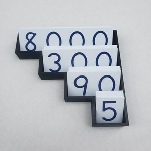 May include: A black plastic number holder with white cards displaying the numbers 8, 000, 300, 90, and 5.