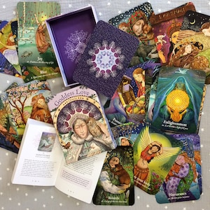 May include: A Goddess Love Oracle card deck with a purple box and guidebook. The cards feature colourful illustrations of women and nature scenes. The deck includes cards with titles like "Joy," "Bliss," and "Enlightenment."