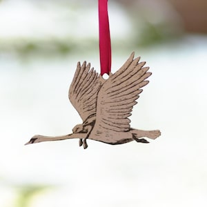 Op de afbeelding: Een houten ornament in de vorm van een vliegende gans met een rood lint aan de bovenkant.