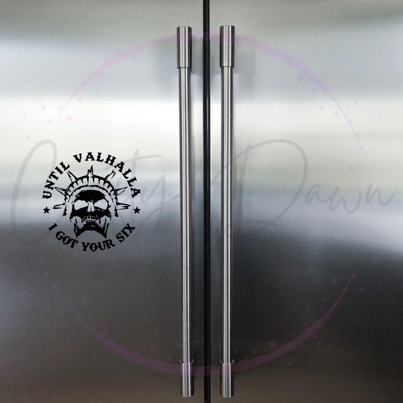 May include: A stainless steel refrigerator with two doors and black handles. A black and white sticker with the text "Until Valhalla I got your six" is on the left door.