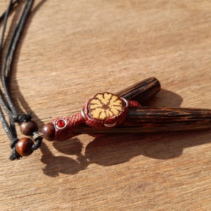 Peut inclure: Un collier en bois avec un pendentif à motif brun et noir. Le pendentif a un motif de fleur rouge et jaune avec un petit bijou rouge au centre.