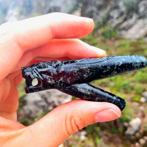 Op de afbeelding: Een groene en zwarte stenen sculptuur van een wolfskop, met ingewikkelde details en een klein gaatje in de mond. De sculptuur heeft de vorm van een pijp, met een lange, dunne steel.