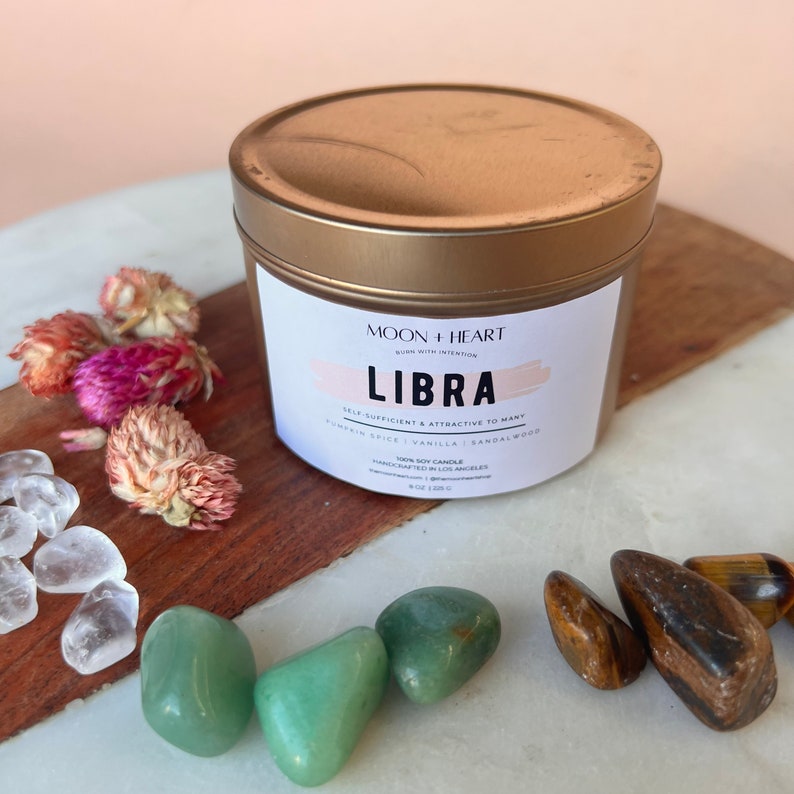 May include: Gold candle tin with a white label that reads "Moon + Heart Burn with Intention Libra Self-Sufficient & Attractive to Many Pumpkin Spice | Vanilla | Sandalwood 100% Soy Candle Handcrafted in Los Angeles 8 oz (226 g)"