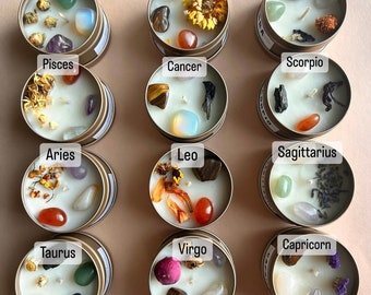 May include: Twelve small candles in gold tins, each representing a different zodiac sign. Each candle features a white wax base with various crystals, dried flowers, and other decorative elements.