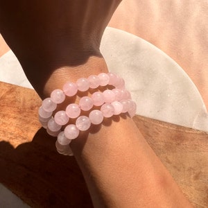 Puede incluir: Un conjunto de tres pulseras de cuarzo rosa. Las pulseras están hechas de cuentas redondas y se llevan en la muñeca.