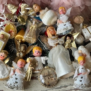 May include: A collection of vintage Christmas ornaments, including angel figurines, bells, and decorative shapes. The ornaments feature gold, white, and pastel colors, with intricate details and a nostalgic aesthetic. Some ornaments have small doll faces.