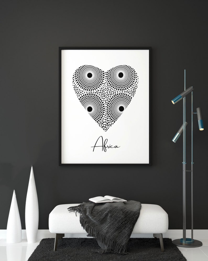 May include: Black and white print of a heart shape made of circles with the word "Africa" underneath. The print is framed and hanging on a black wall above a white bench with a grey blanket.