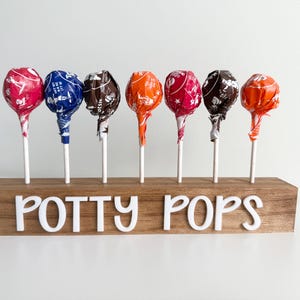 May include: A wooden stand with the words "Potty Pops" on the front. Seven colorful lollipops are displayed in the stand.