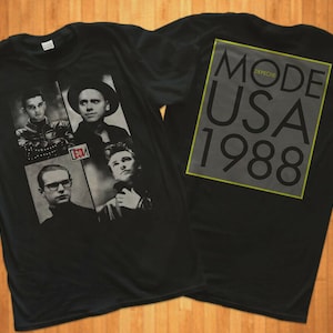 Op de afbeelding: Zwart T-shirt met een bandgrafiek met vier mannen in zwart-wit. De tekst "MODE DEPECHE USA 1988" is gedrukt op de achterkant van het shirt.
