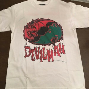 May include: White t-shirt with a red, green, and black graphic of a demon with wings and the word "DEVILMAN" in red and black letters. The text "DYNAMIC PLANNING" is written in small letters below the graphic.