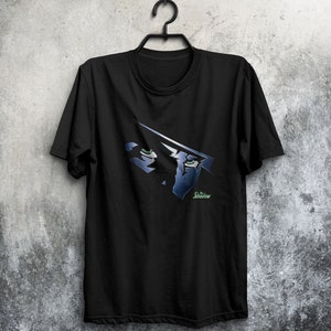 May include: Black t-shirt with a graphic of the Shadow's eyes and the text "The Shadow" in green.