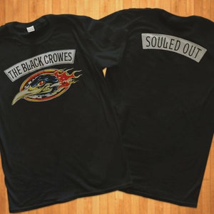 以下が含まれることがあります： 黒いTシャツに、炎の中に鳥が描かれた白いグラフィックと「The Black Crowes」の文字がプリントされています。Tシャツの背面には、「Souled Out」の文字が書かれた白いパッチが付いています。