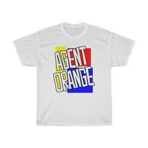 Pode incluir: Camiseta branca com um design gráfico das palavras "AGENT ORANGE" em letras brancas sobre um fundo de quadrados amarelos, vermelhos e azuis.