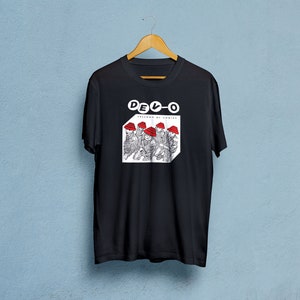 Op de afbeelding: Zwart T-shirt met een witte afbeelding van de band DEVO. De afbeelding toont de bandleden met rode hoeden en de tekst "Freedom of Choice".