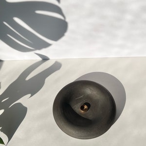 May include: A black ceramic incense holder with a small hole in the center. The holder is round and has a slightly raised edge.