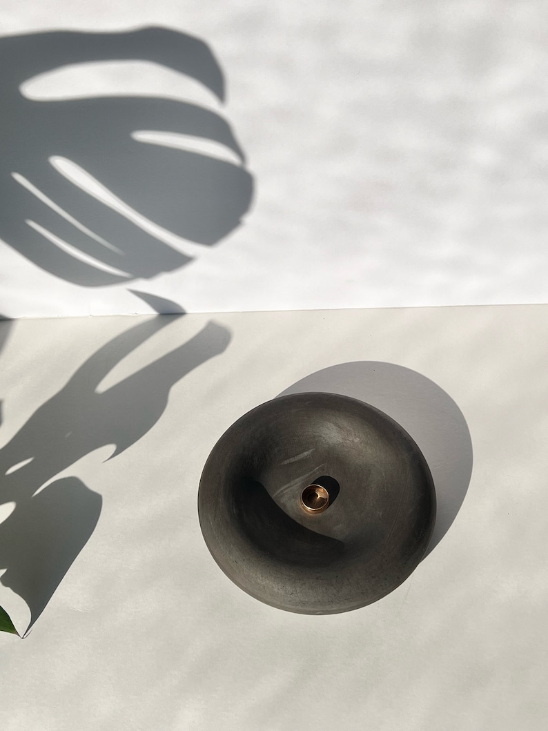 May include: A black ceramic incense holder with a small hole in the center. The holder is round and has a slightly raised edge.