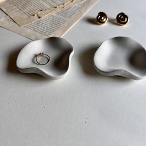 Peut inclure: Deux plats en c&eacute;ramique blancs de forme irr&eacute;guli&egrave;re. Un plat contient une bague en or.
