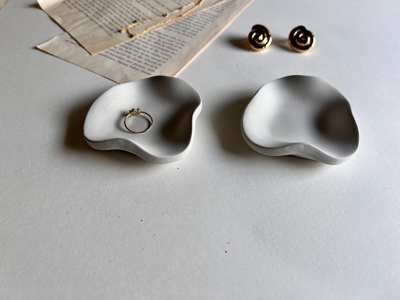 Peut inclure: Deux plats en c&eacute;ramique blancs de forme irr&eacute;guli&egrave;re. Un plat contient une bague en or.
