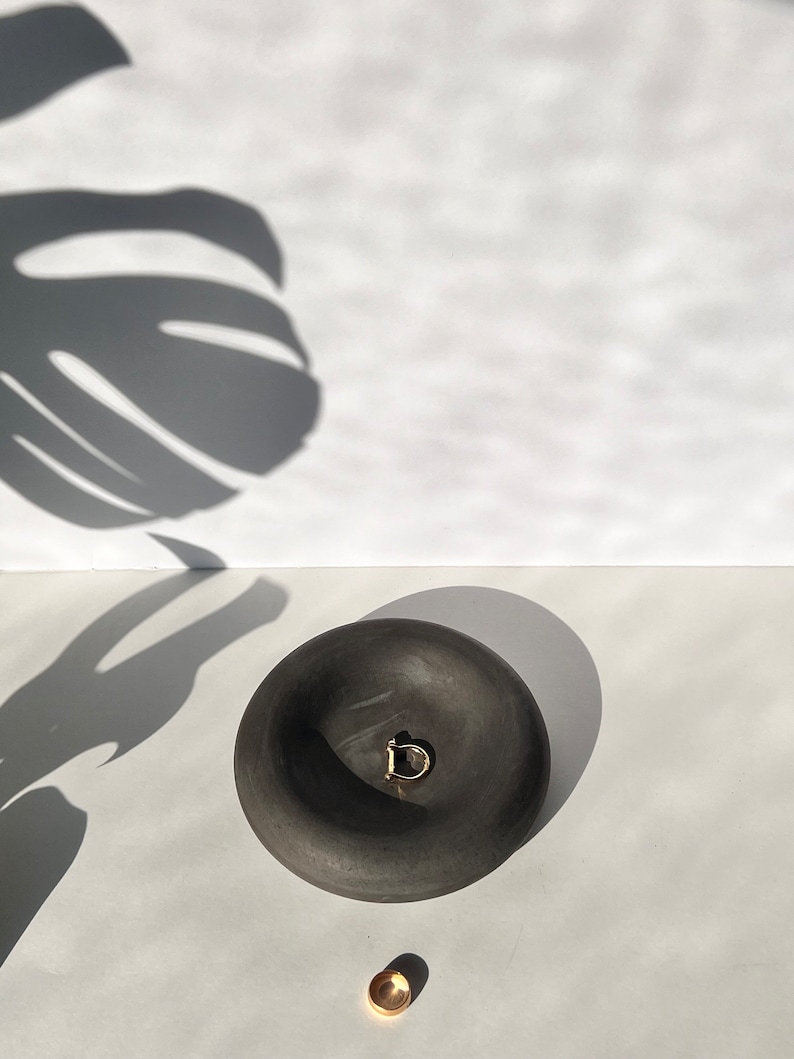 May include: A black ceramic bowl with a rounded shape and a gold ring inside. The bowl is sitting on a white surface.