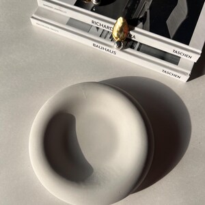 May include: A white ceramic bowl with a smooth, rounded surface. The bowl is sitting on a white surface.