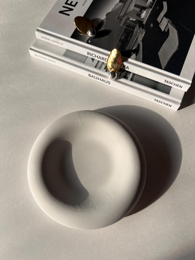 May include: A white ceramic bowl with a smooth, rounded surface. The bowl is sitting on a white surface.
