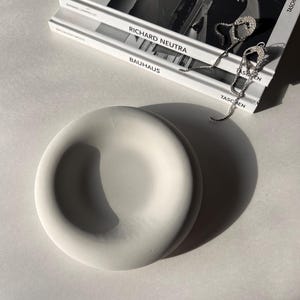 May include: A white ceramic dish with a rounded, slightly raised rim. The dish is sitting on a white surface.